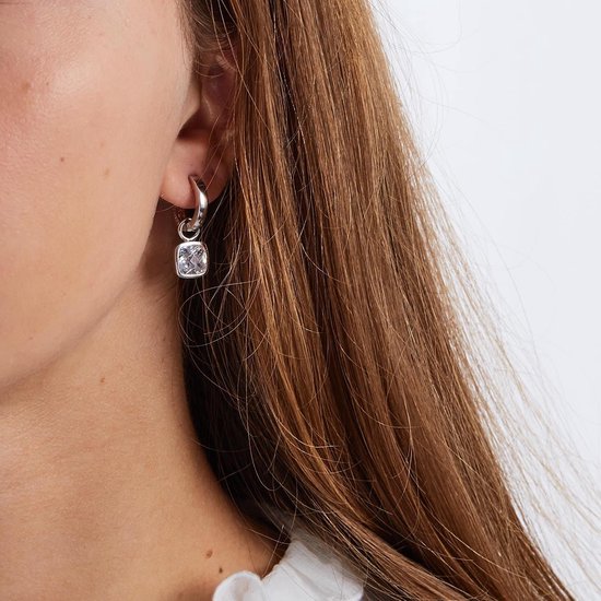 Model draagt een zilveren oorbel met een vierkante, witte hanger.