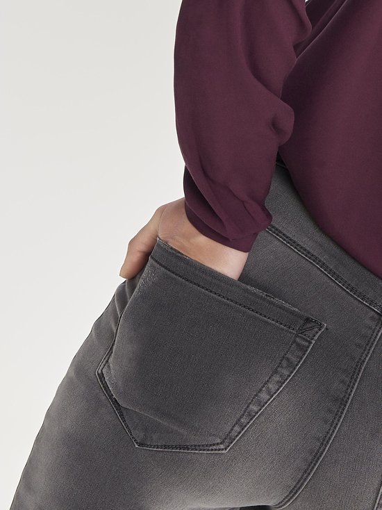 Detail van de achterzak van een grijze skinny jeans, gedragen door een model.