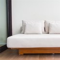 Een witte loungebank met houten frame, voorzien van witte kussens.