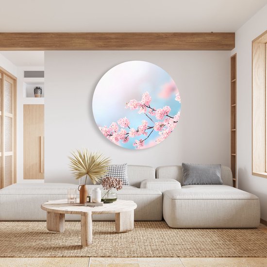 Cercle mural rond avec des branches de fleurs roses sur fond bleu ciel doux et rose, au-dessus d'un canapé clair.