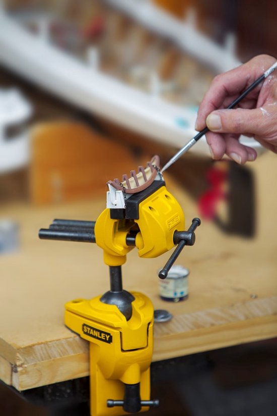 Gele multifunctionele boorklem van Stanley die een model vasthoudt, terwijl iemand het schildert.