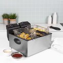 Zilverkleurige dubbele frituurpan op een aanrecht, met mandjes, frietjes, kipnuggets en dipsauzen.