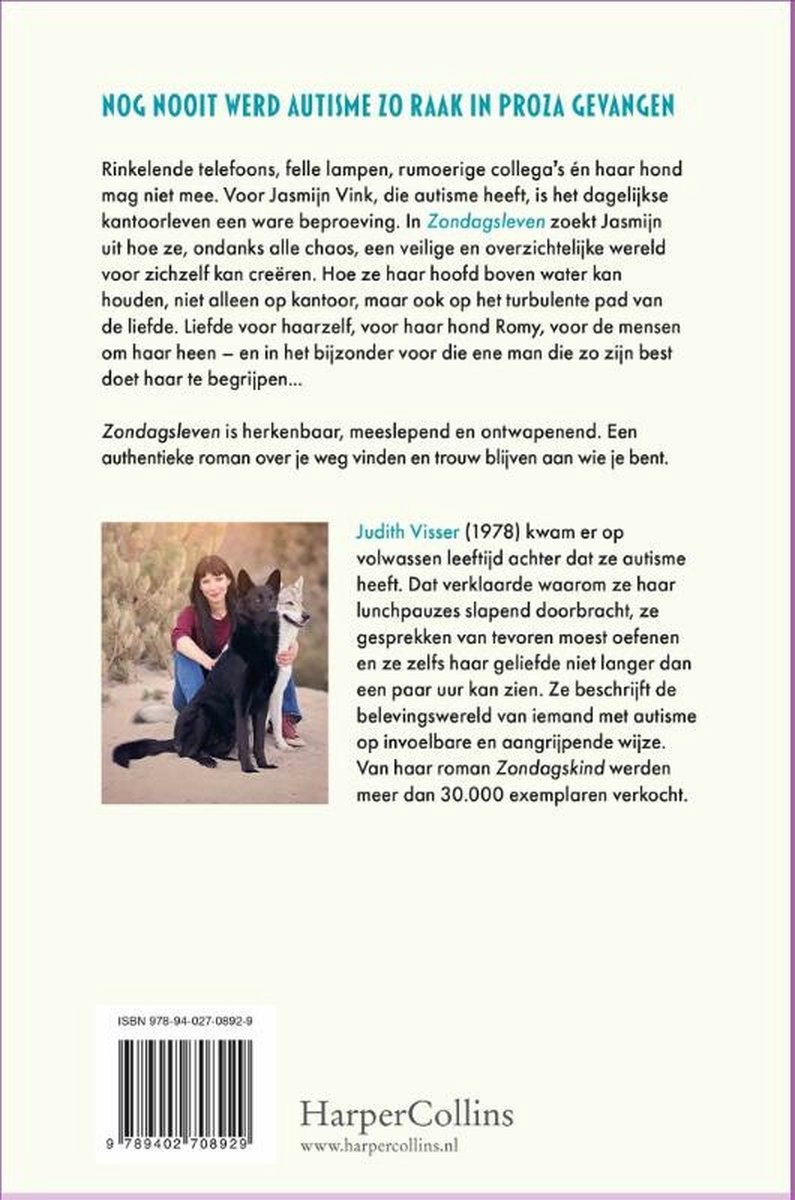 Een vrouw zit op de grond naast twee honden, een zwarte en een grijze. Ze draagt een blauwe spijkerbroek en een bruine jas.