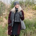 Model in grijze gebreide sjaal, muts en handschoenen. Draagt een bordeauxrode vest en zwarte jurk.