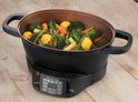Zwarte multicooker met gestoomde groenten: broccoli, bloemkool, wortel en peultjes.
