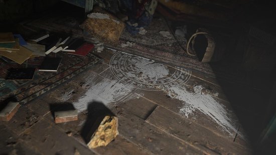 Een houten vloer met boeken, een tapijt met een cirkelvormig symbool en witte verf.