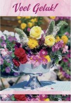 Veel geluk! Een bijzondere wenskaart met een vaas vol diverse bloemen op tafel. Op de achtergrond zijn ook bloemen te zien. De wenskaart is inclusief envelop en in folie verpakt.