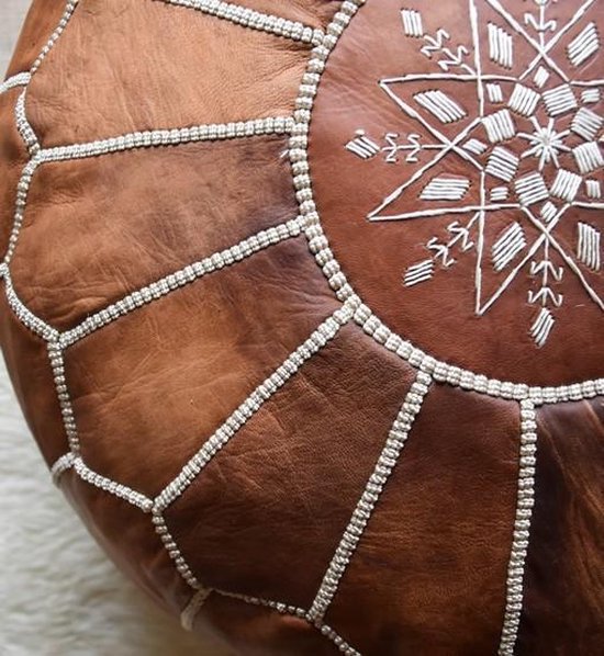 Close-up van een cognacbruine lederen poef met gedetailleerd wit stikwerk en een centraal stervormig motief.