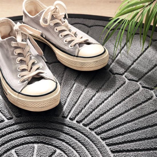 Close-up van een grijze deurmat met een reliëfpatroon, waarop lichtgrijze sneakers zijn geplaatst. Het patroon lijkt op stralen uit een cirkel.