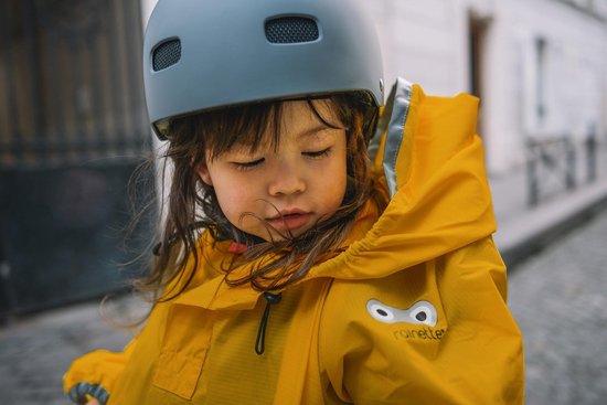 Meisje met helm op, draagt een gele regenjas met Rainette logo.