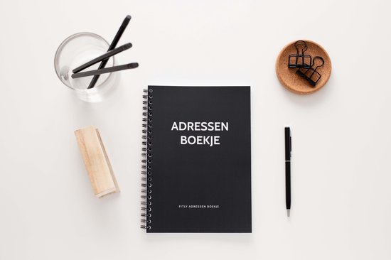 Petit carnet d'adresses noir fermé avec 'ADRESSEN BOEKJE' sur la couverture, entouré d'articles de bureau.