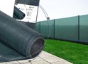 Groen schaduwdoek geplaatst over een hekwerk langs een terras en grasveld, met productinformatie.