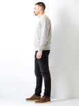 Man in grijze sweater en zwarte jeans, van opzij gezien, met bruine schoenen.
