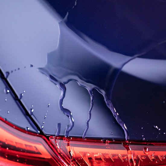 Détailleur liquide violet coulant sur la peinture bleu foncé d'une voiture, avec des gouttes.