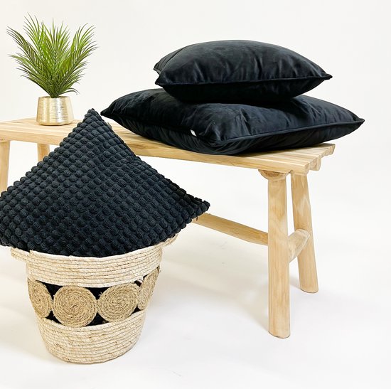 Drie effen zwarte fluwelen kussens op een houten bank, en één zwart kussen met textuur in een mand.
