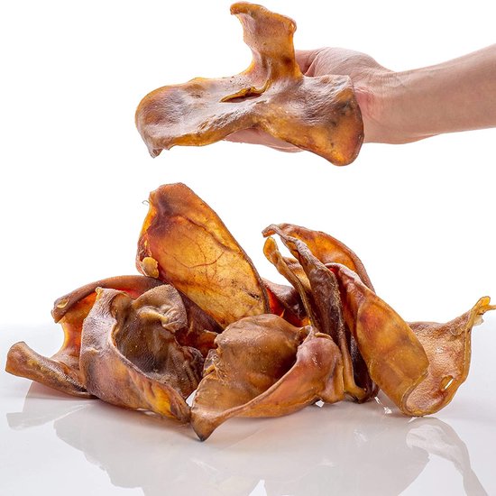 Een hand houdt een gedroogd varkensoor omhoog, met een stapel van soortgelijke oren eronder.