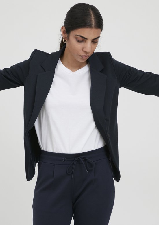 Model in een donkerblauwe blazer en een witte top, met wijd gespreide armen.