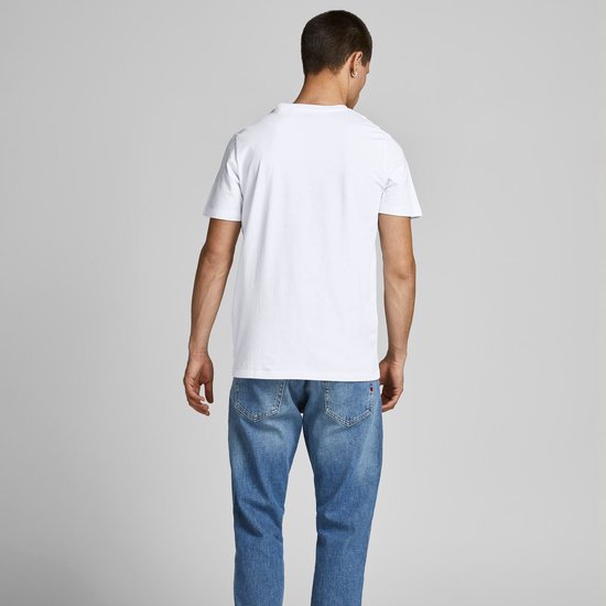 Man draagt een wit T-shirt en een spijkerbroek, kijkend weg.