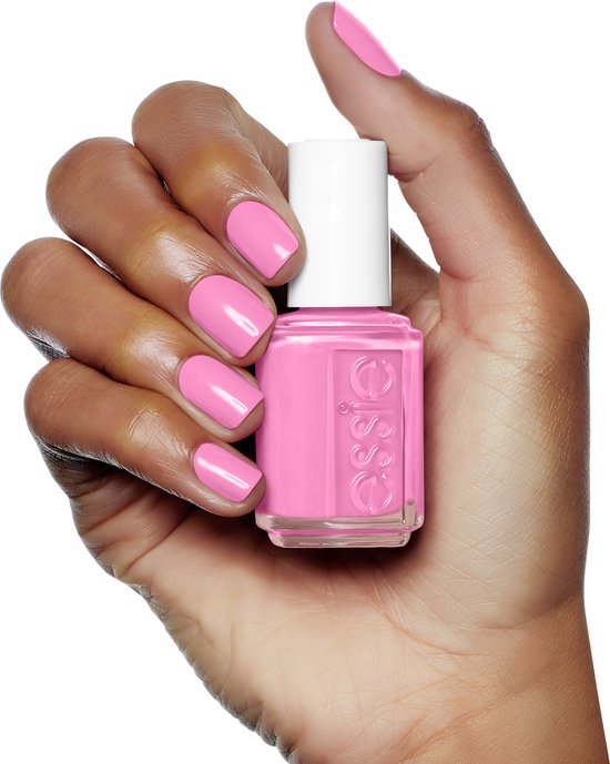 Donkere hand met gelakte nagels in fel roze, met een flesje Essie nagellak.