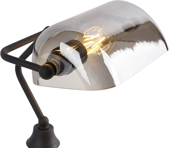 Gros plan de l'abat-jour en verre gris et du bras métallique d'une lampe de banquier.