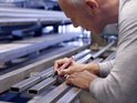 Man meet met een liniaal en kleurt met zwarte edding 3000 marker op metalen staven.