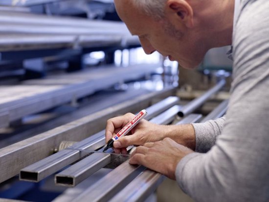 Man meet met een liniaal en kleurt met zwarte edding 3000 marker op metalen staven.