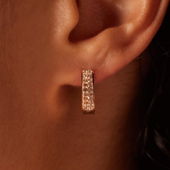 Close-up van een rosekleurige oorbel met kristallen in een oor.
