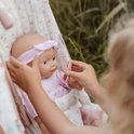 Meisje met blond haar past de hoofdband van een pop in een roze kinderwagen aan.
