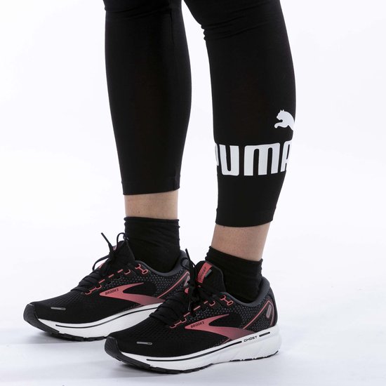 Gedetailleerde close-up van de onderbenen van een vrouw in zwarte leggings met Puma-logo, gedragen met hardloopschoenen.