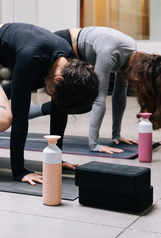 Twee Dopper Insulated drinkflessen in peach en roze op yogamatten.