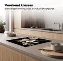 Glazen snijplank met witte en gouden bloemen, op een aanrecht.