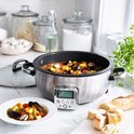 Roestvrijstalen multicooker met glazen deksel, gevuld met stoofpot, naast brood.