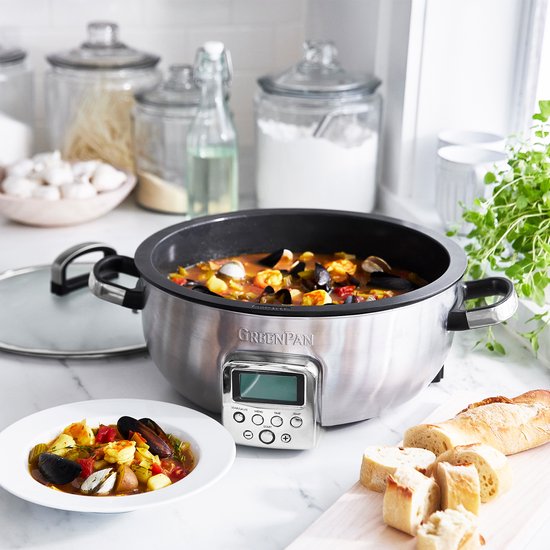 Roestvrijstalen multicooker met glazen deksel, gevuld met stoofpot, naast brood.