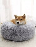 Een Shiba Inu hond ligt in een zacht, rond grijs hondenkussen met opstaande rand.
