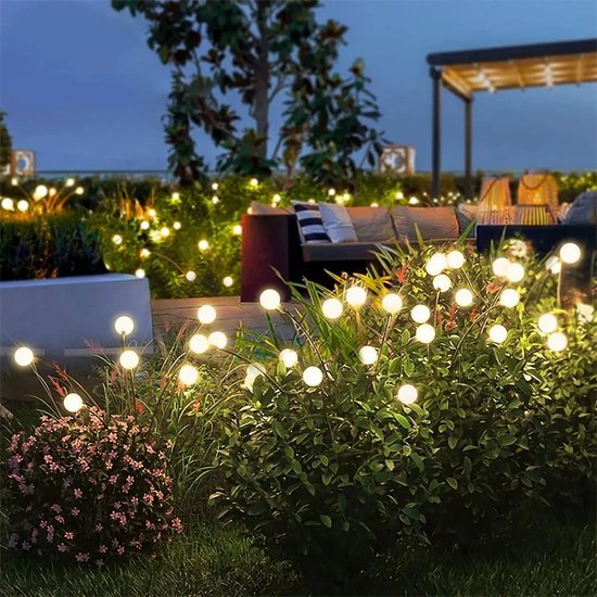 Un jardin joliment éclairé le soir avec des lampes Boncy lucioles, disposées dans des buissons et des plantes.