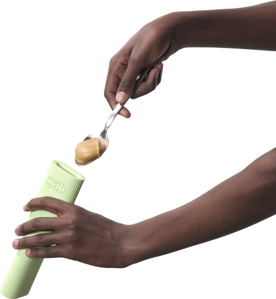 Handen vullen lichtgroen, geribbeld "earth rated" kauwspeeltje met pindakaas uit een lepel.