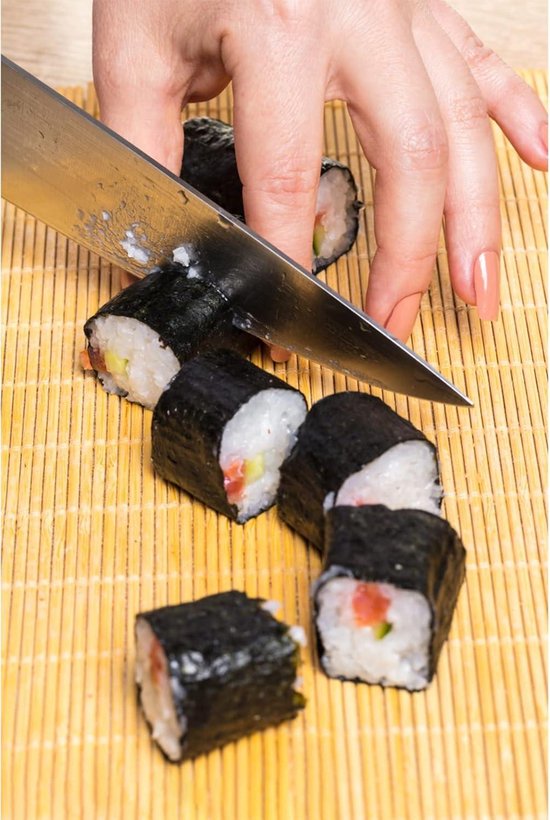 Een hand snijdt sushirollen met een mes op een bamboemat.