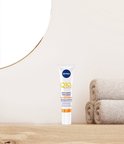 NIVEA Q10 plus C Energy oogcontourcrème staat op een houten plank naast opgevouwen handdoeken en een spiegel.