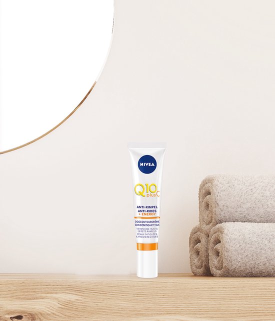 NIVEA Q10 plus C Energy oogcontourcrème staat op een houten plank naast opgevouwen handdoeken en een spiegel.