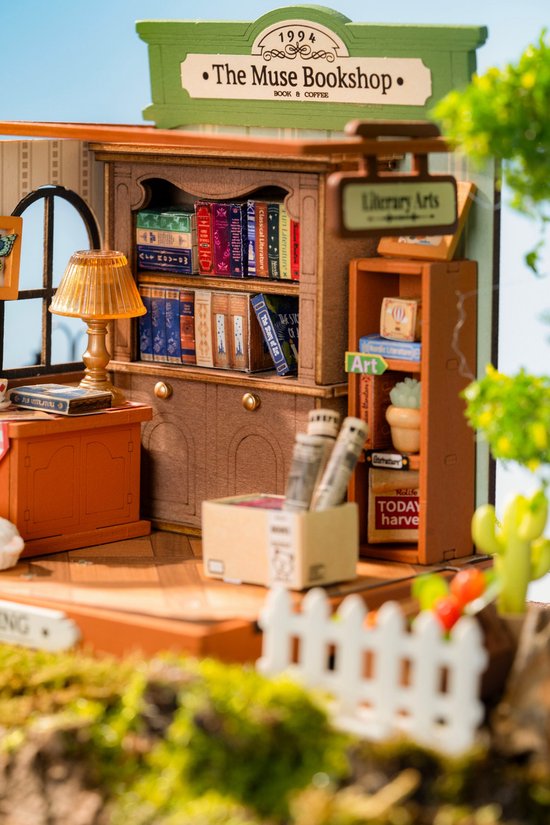 Miniatuur boekenwinkel "The Muse Bookshop" met boeken, lamp, kat en een kleine witte tuinhek.