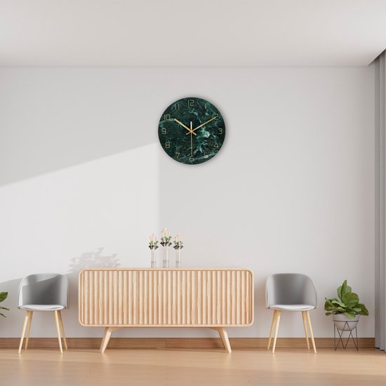 Groene marmerlook wandklok met gouden wijzers, boven een houten kast.