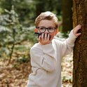 Een jongen in een bos, achter een boom, met een walkie talkie bij zijn mond.