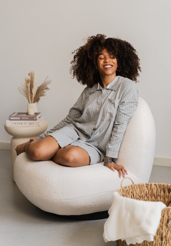 Model in grijze gestreepte pyjama met lange mouwen, zittend op een witte fauteuil.