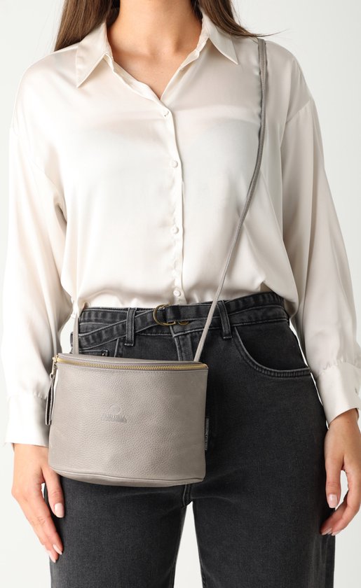 Vrouw met grijze leren crossbody tas, gedragen over de schouder.