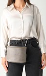 Vrouw met grijze leren crossbody tas, gedragen over de schouder.
