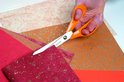 Oranje Fiskars schaar knipt in rood papier met bloemenpatroon, met bruin papier.