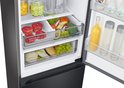 Close-up van de inhoud van de zwarte Samsung koelkast: verse groenten zoals broccoli en sla, fruit zoals druiven en mango, en vleeswaren in de 'Optimal Fresh+' en 'Humidity Fresh+' lades.