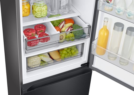 Close-up van de inhoud van de zwarte Samsung koelkast: verse groenten zoals broccoli en sla, fruit zoals druiven en mango, en vleeswaren in de 'Optimal Fresh+' en 'Humidity Fresh+' lades.
