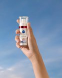 Hand houdt Nivea Cellular Luminous630 Anti-Age & Anti-Spot serum vast tegen een blauwe hemel.
