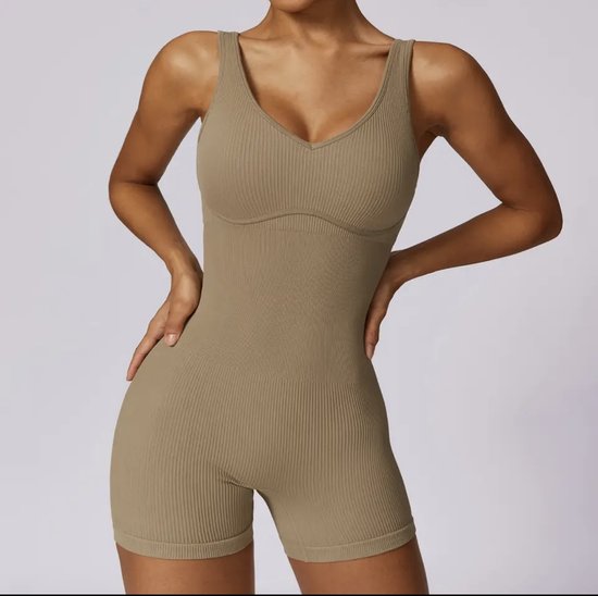 Model in zandkleurig, nauwsluitend ribgebreid sportpak met korte broek en V-hals. Handen op de heupen.